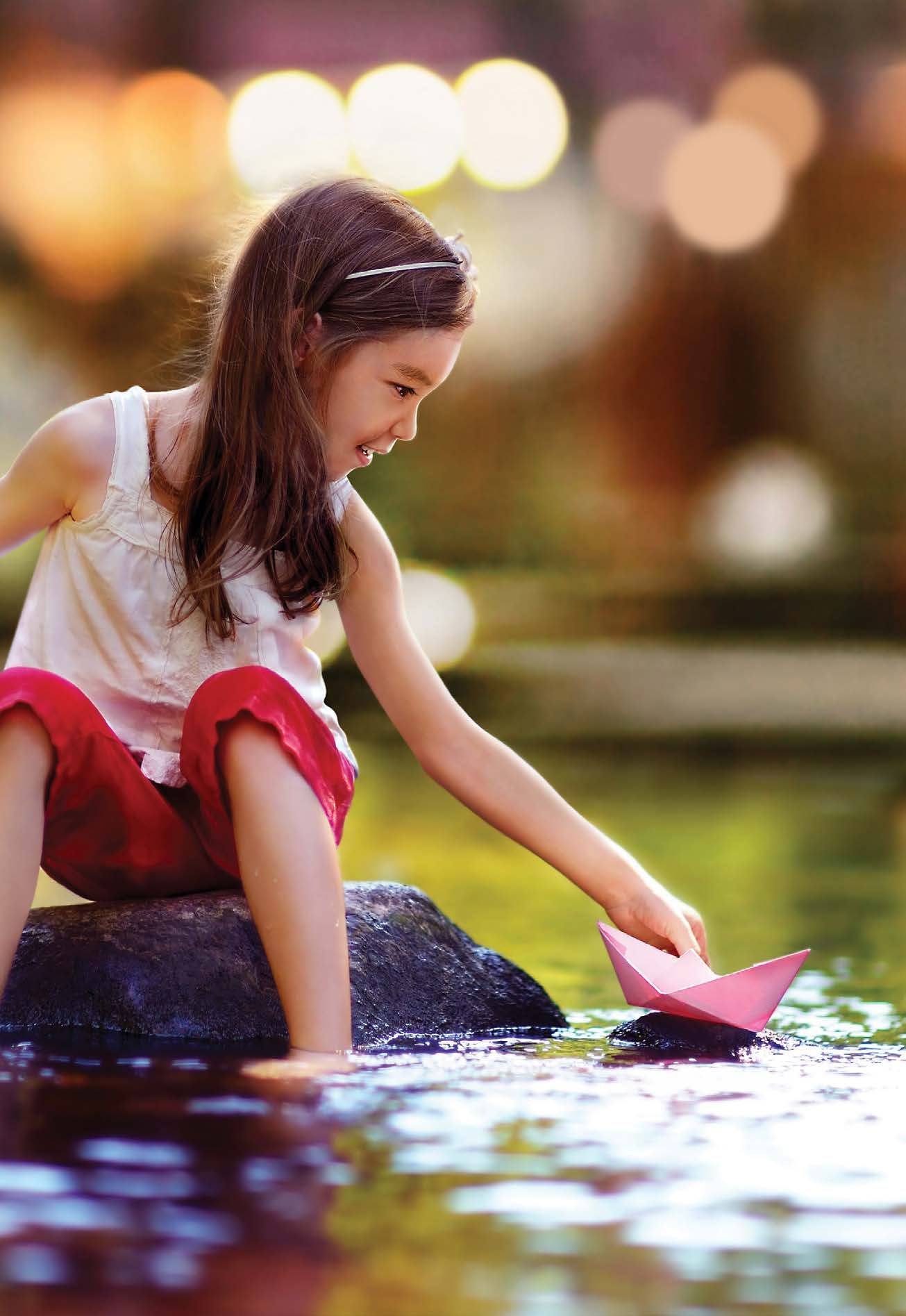 A child playing with a paper boat in the stream